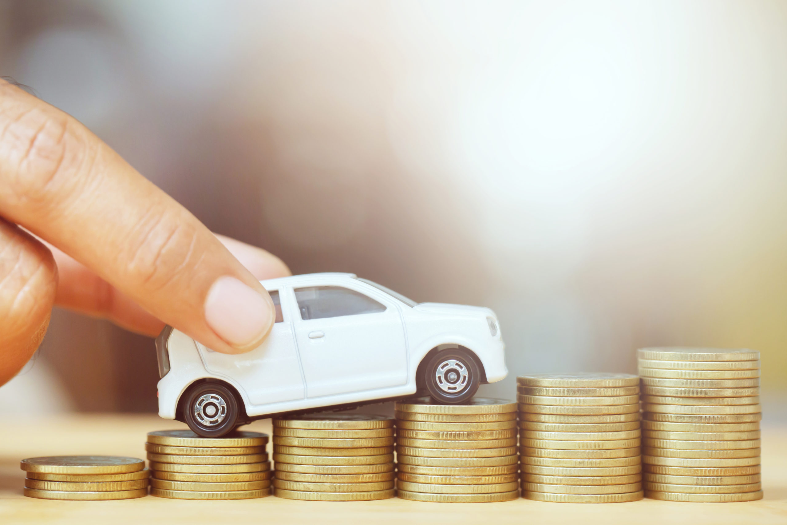 Business man and close up hand holding model of toy car on over a lot money of stacked coins – insurance, loan and buying car finance concept. buy and installments down payment a car.